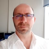 Man with glasses and goatee wearing white shirt in an office setting, looking at camera